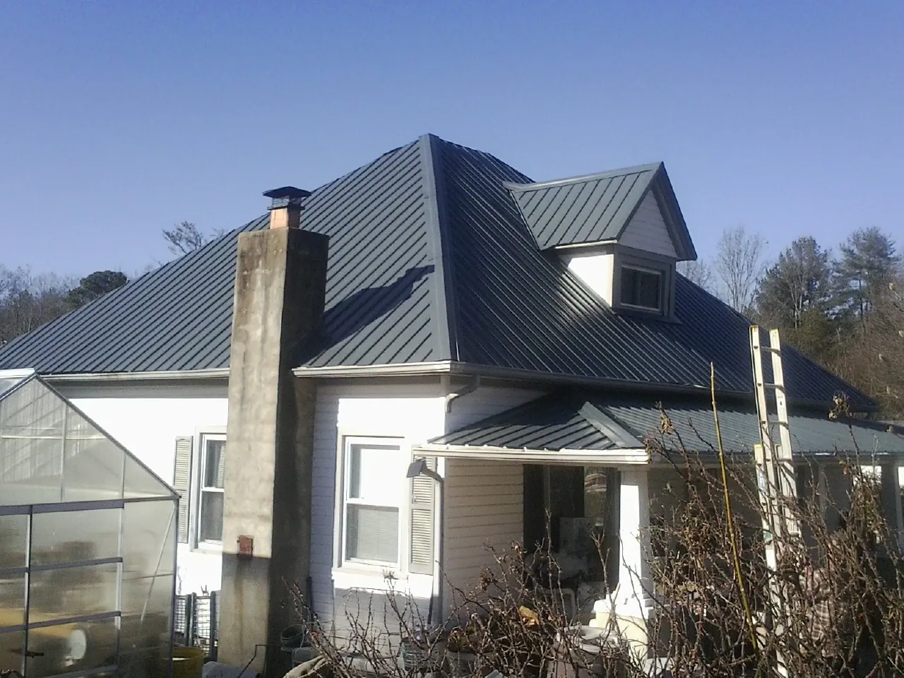 Dark blue standing seam metal roof on a white farmhouse with dormer — Slate & Tile Roof Repair by Roofing Brothers in La Fayette