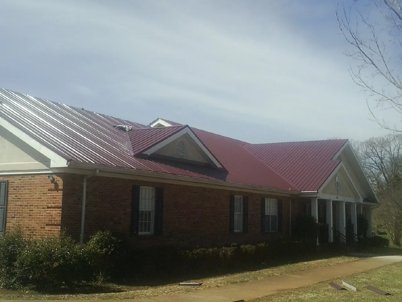 Red metal roof with gabled entries on a long brick building, from a Hail Damage Roof Repair job in La Fayette