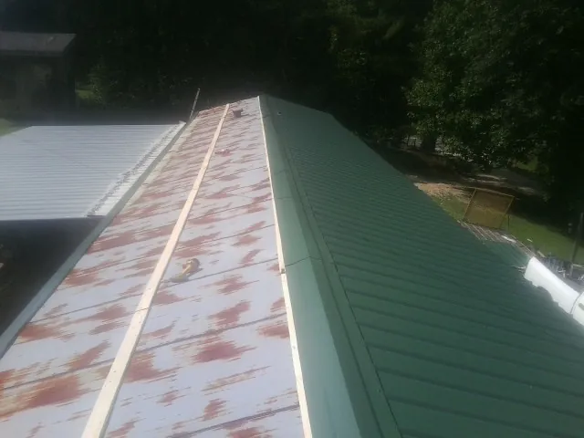 Old rusted panels beside newly installed green metal roofing in La Fayette