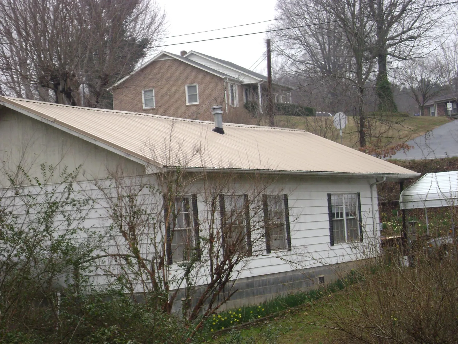 Tan metal roof on a white sided house set into a hillside — Commercial Roofing by Roofing Brothers in La Fayette